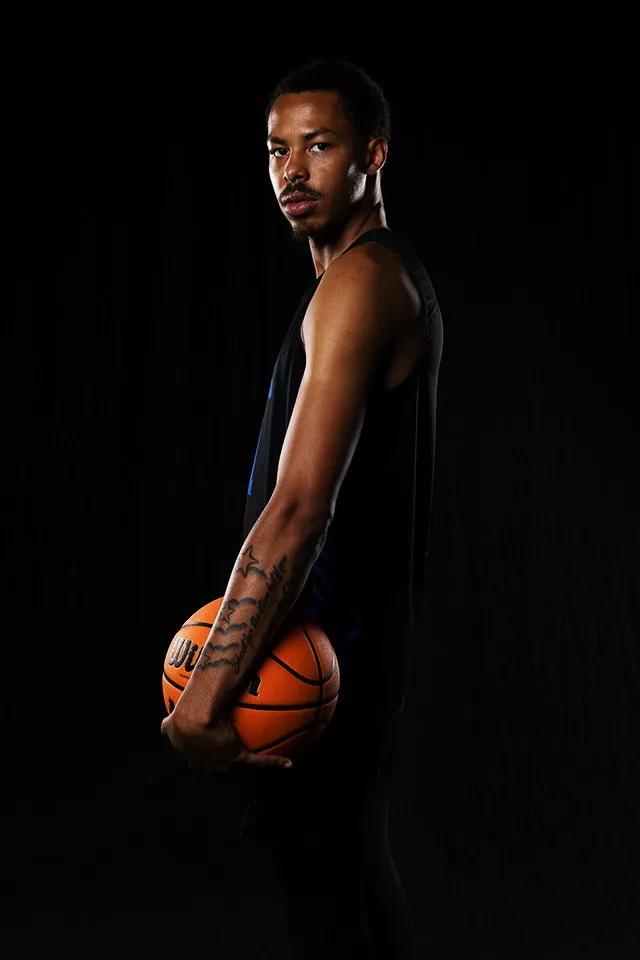 A basketball player poses against a dark background.