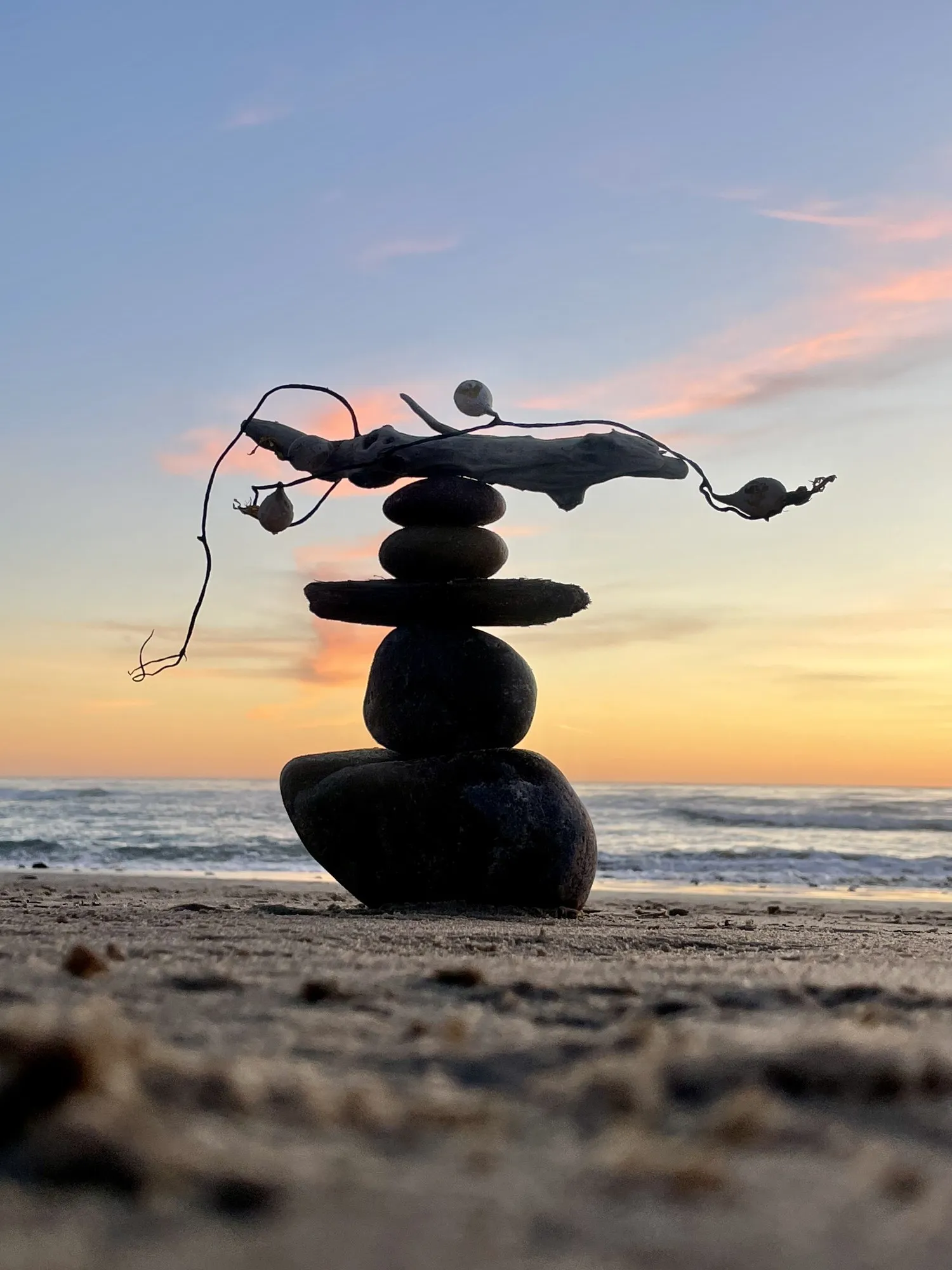 A branch balances across a stone stack at the edge of the sea.
