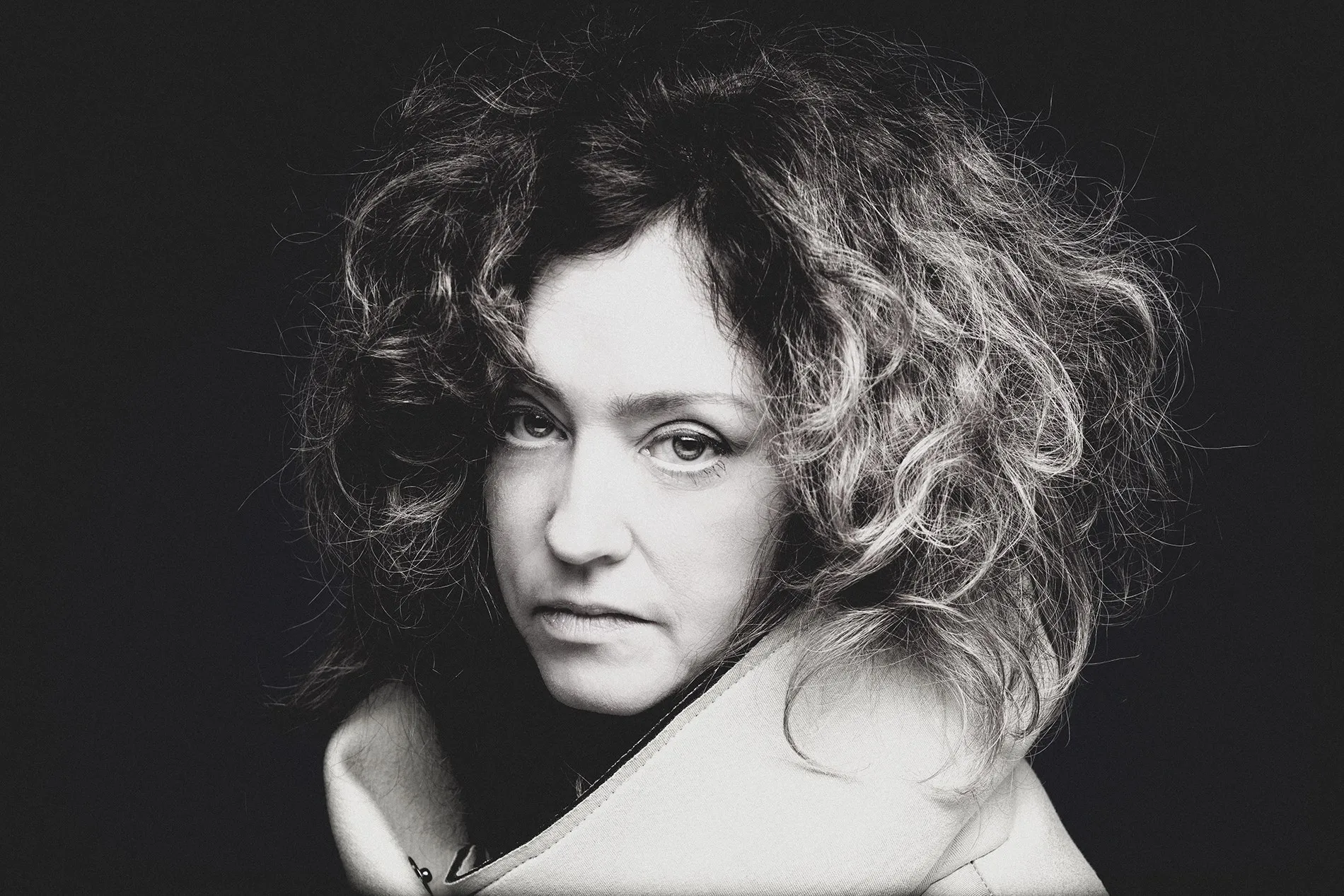 A curly-haired woman looks toward the camera in a black-and-white portrait.