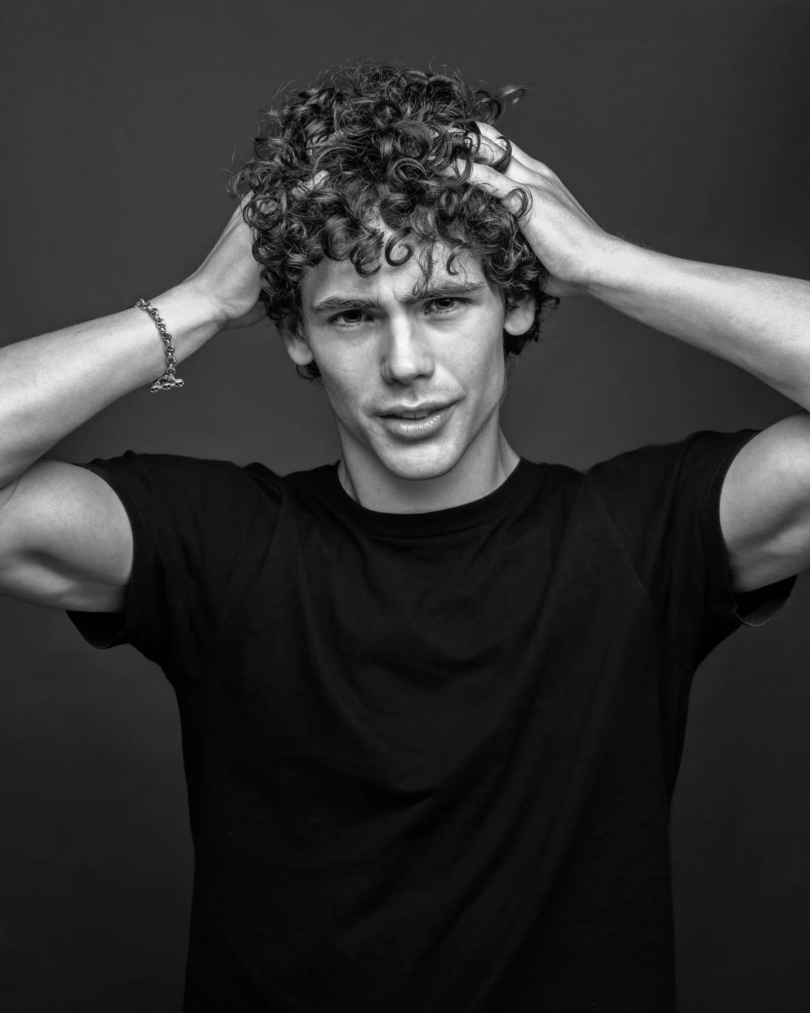 A curly-haired young man holds his head in a dramatic black-and-white studio portrait.