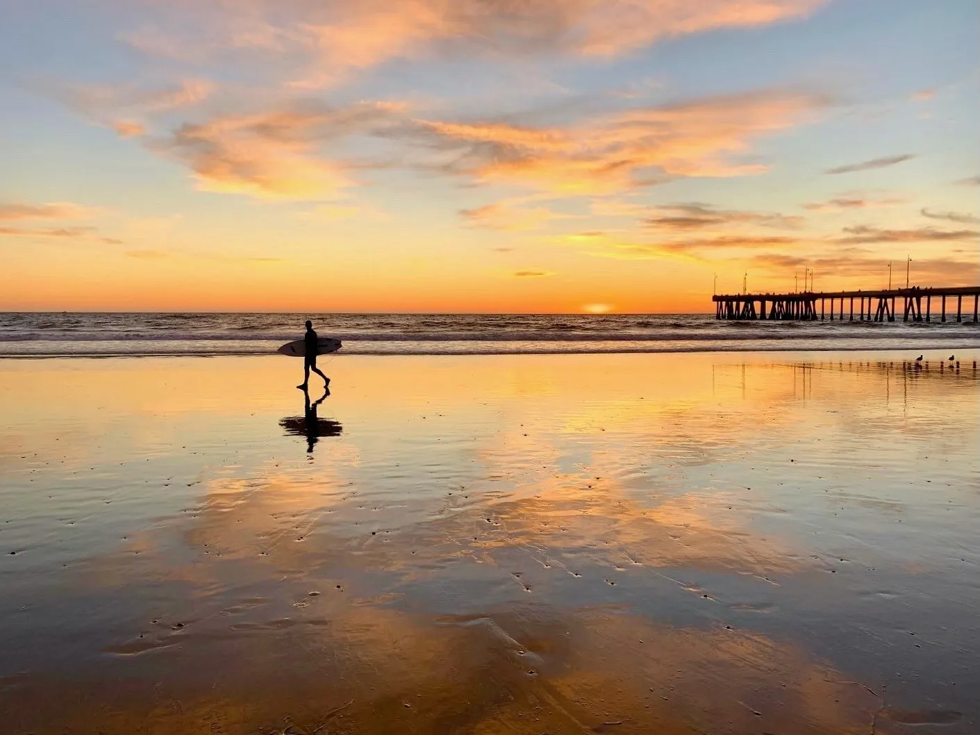 A figure beneath the pier at sunset. A beach observation made in the changing evening light.
