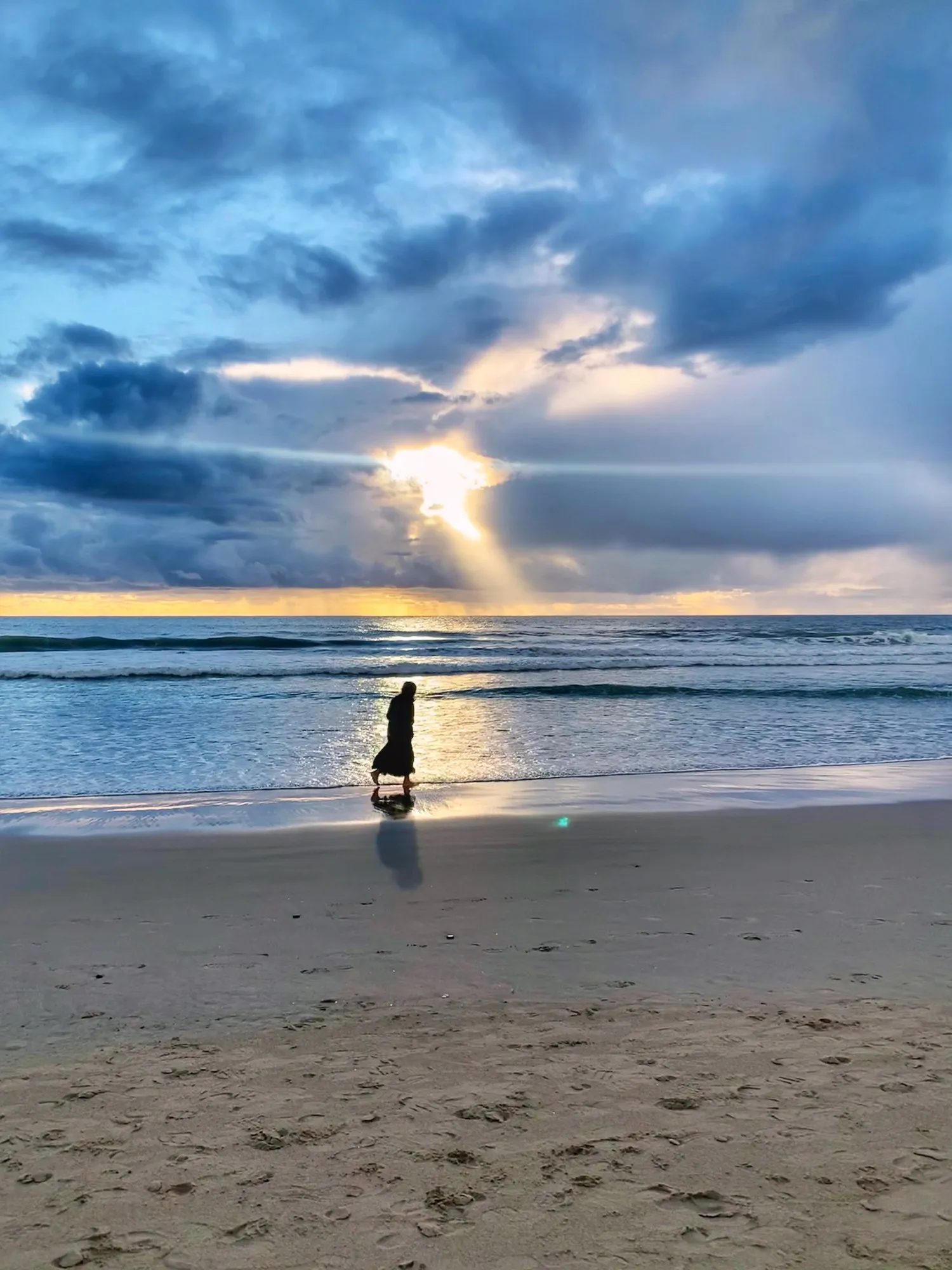 A figure on the shoreline beneath clouds. A beach observation made in the changing evening light.