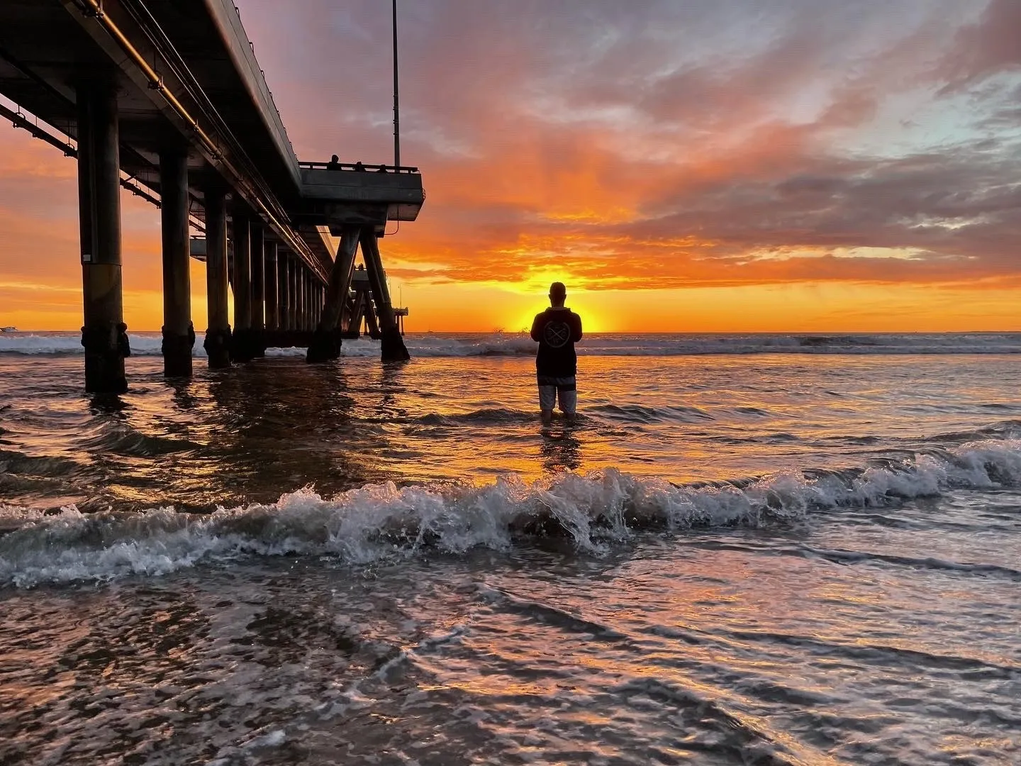 A figure stands beneath the pier. A beach observation made in the changing evening light.