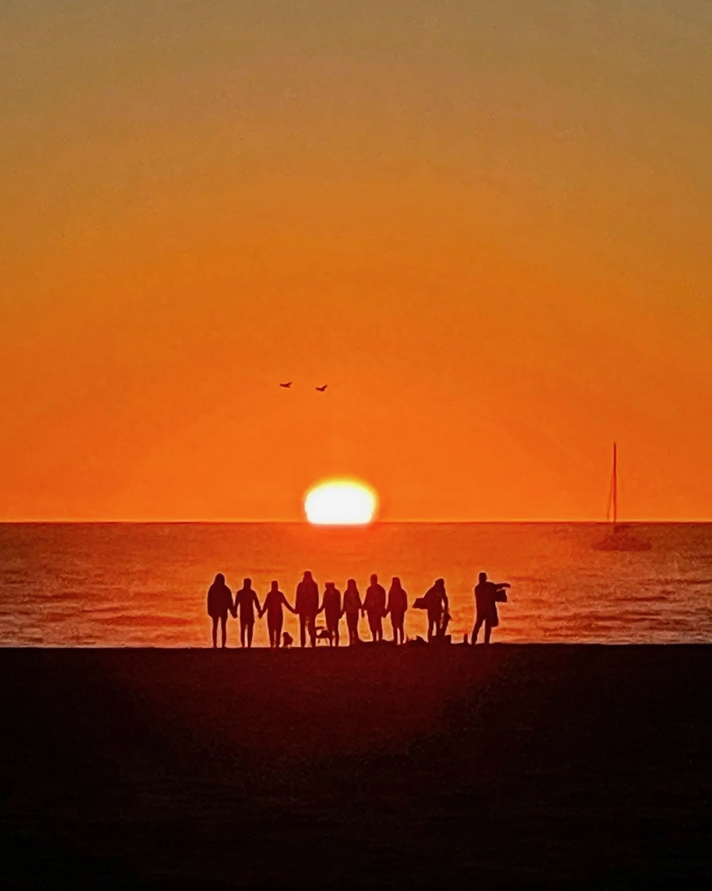 A group watches the sunset. A beach observation made in the changing evening light.