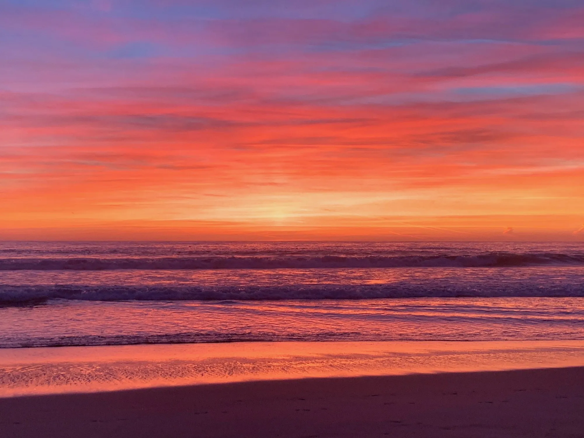 Bands of vivid orange and rose clouds above the sea