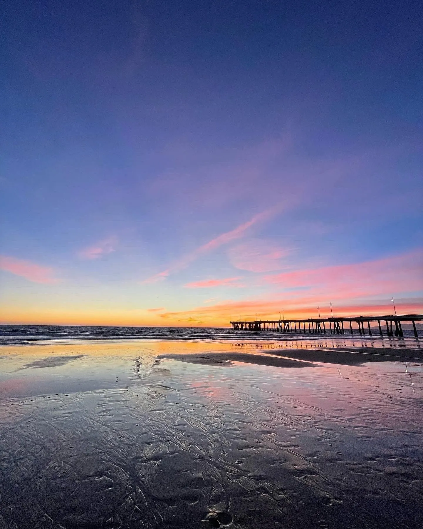 A wide violet sky above a quiet shoreline and pier