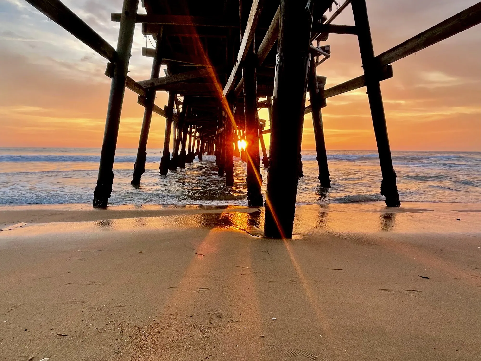 Sunlight shining between the dark supports of a pier