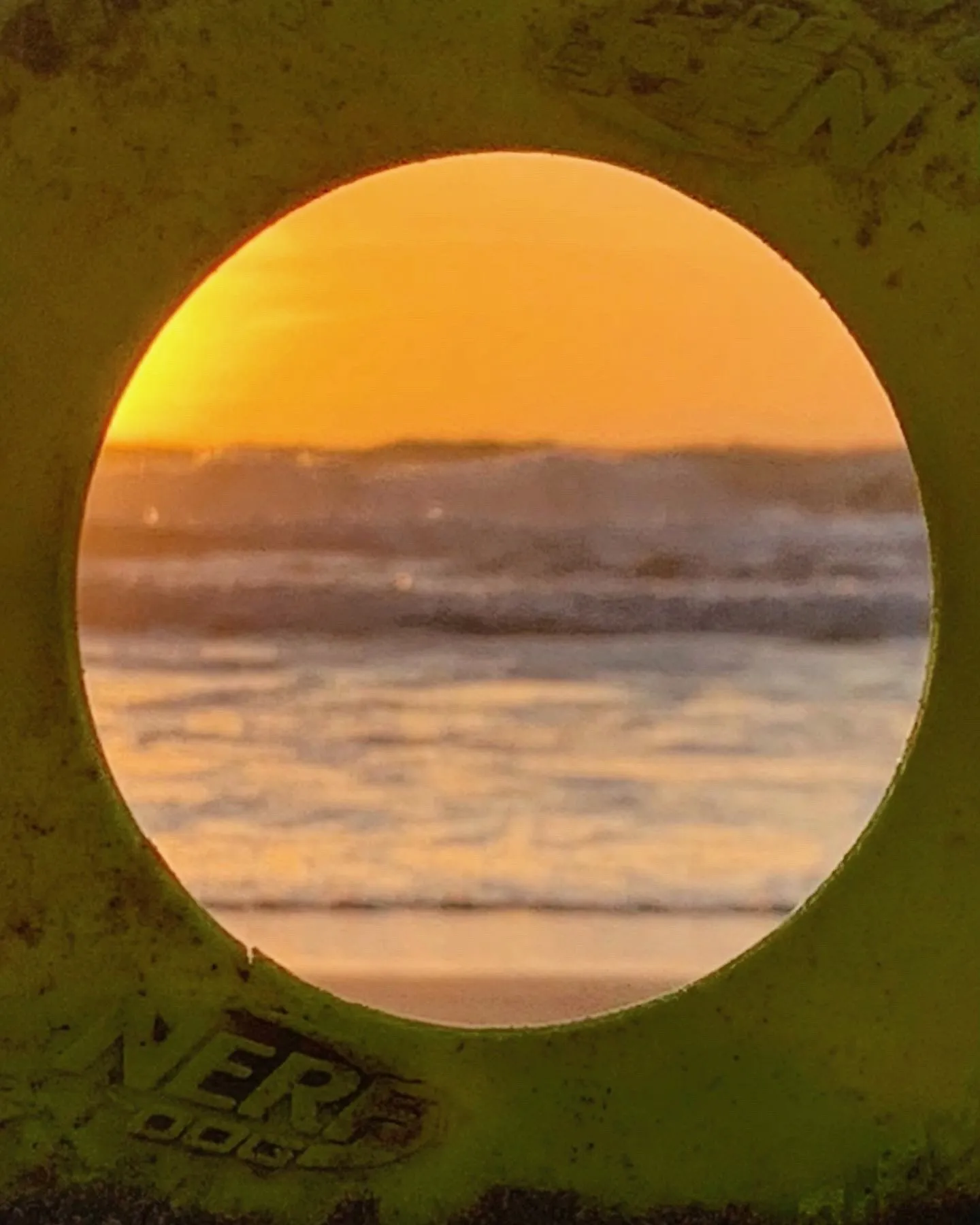 The low sun is framed by a circular opening above the surf.