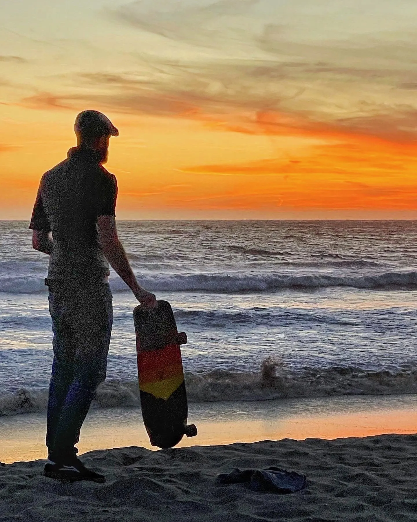 A man carries a bodyboard toward the ocean beneath an orange sky.