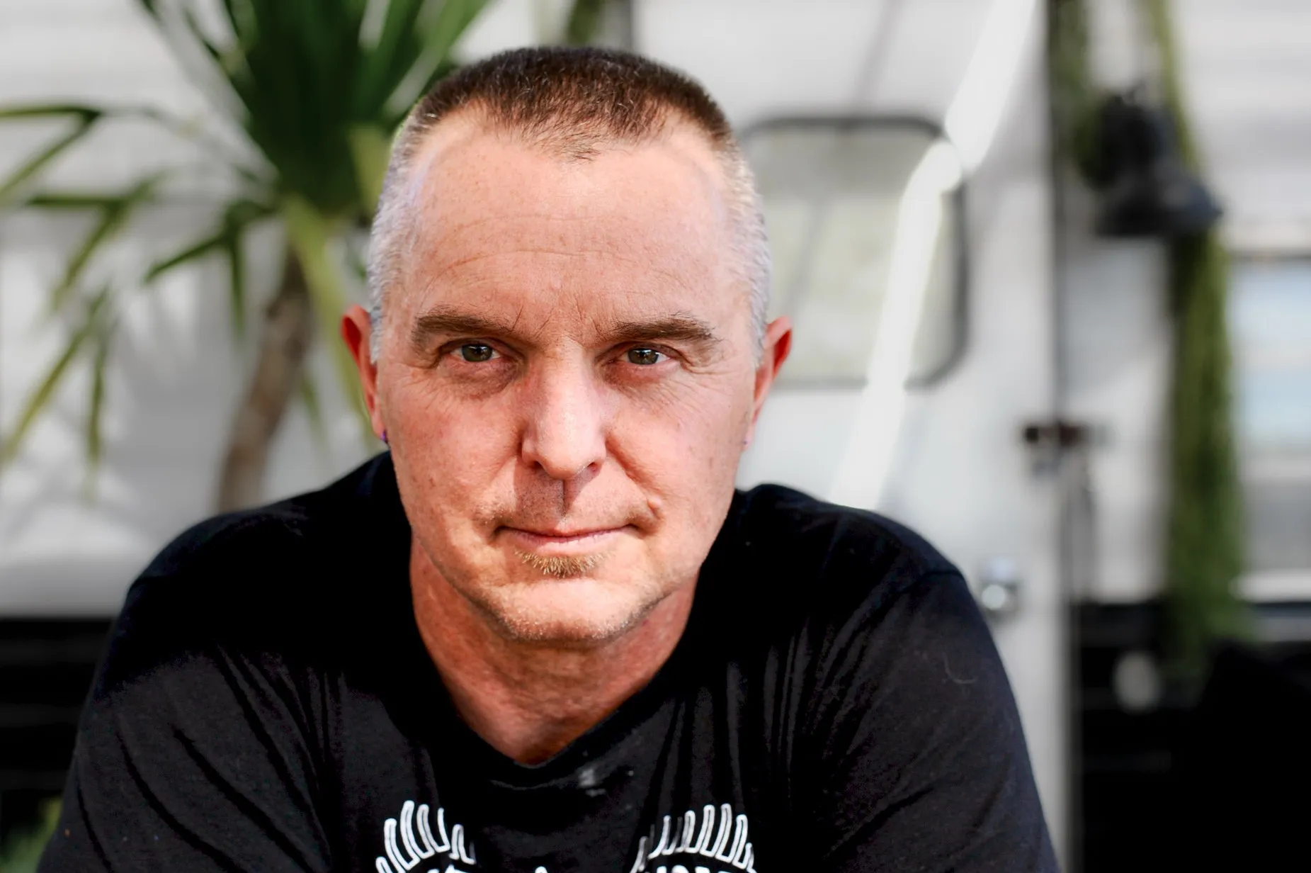 A man in a black shirt leans toward the camera in a softly lit interior.