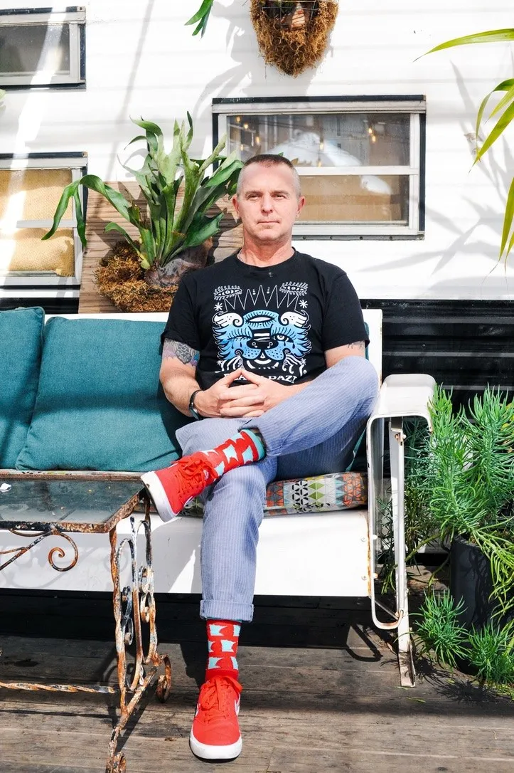 A man sits in a chair outside a storefront with his legs crossed.