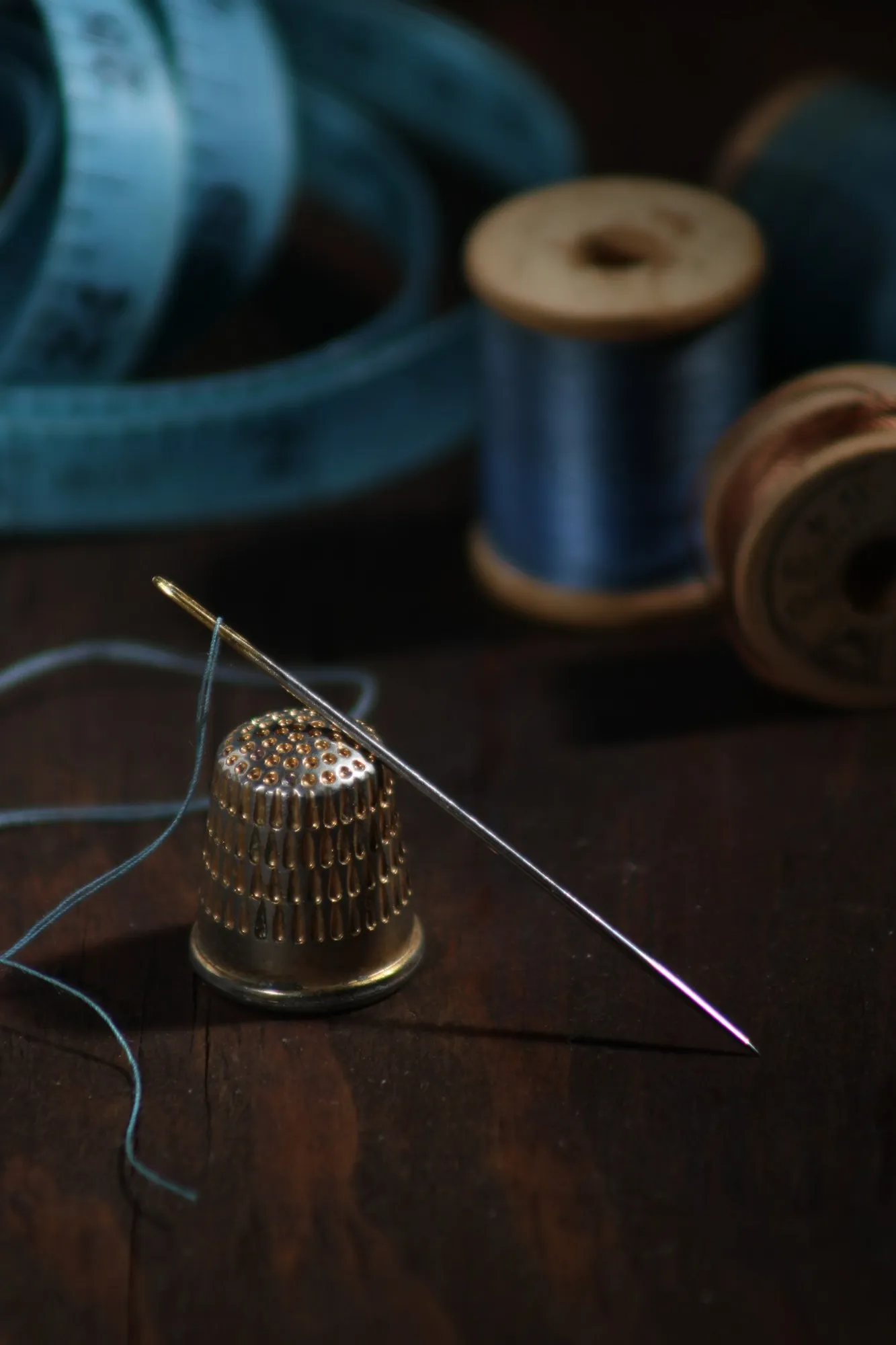 A needle, thread, and thimble rest on a dark blue work surface.