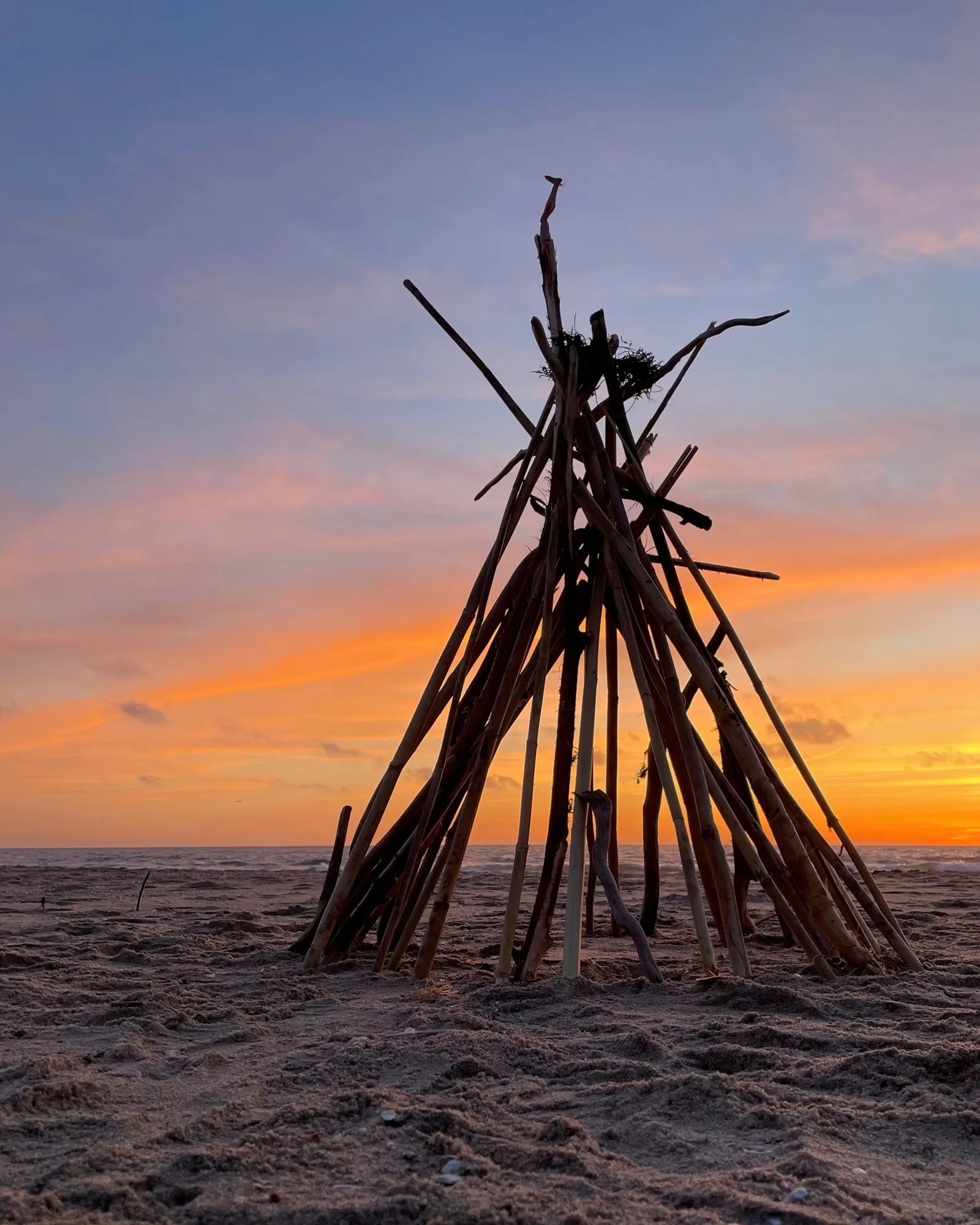 A tall driftwood structure silhouetted against orange and violet evening light