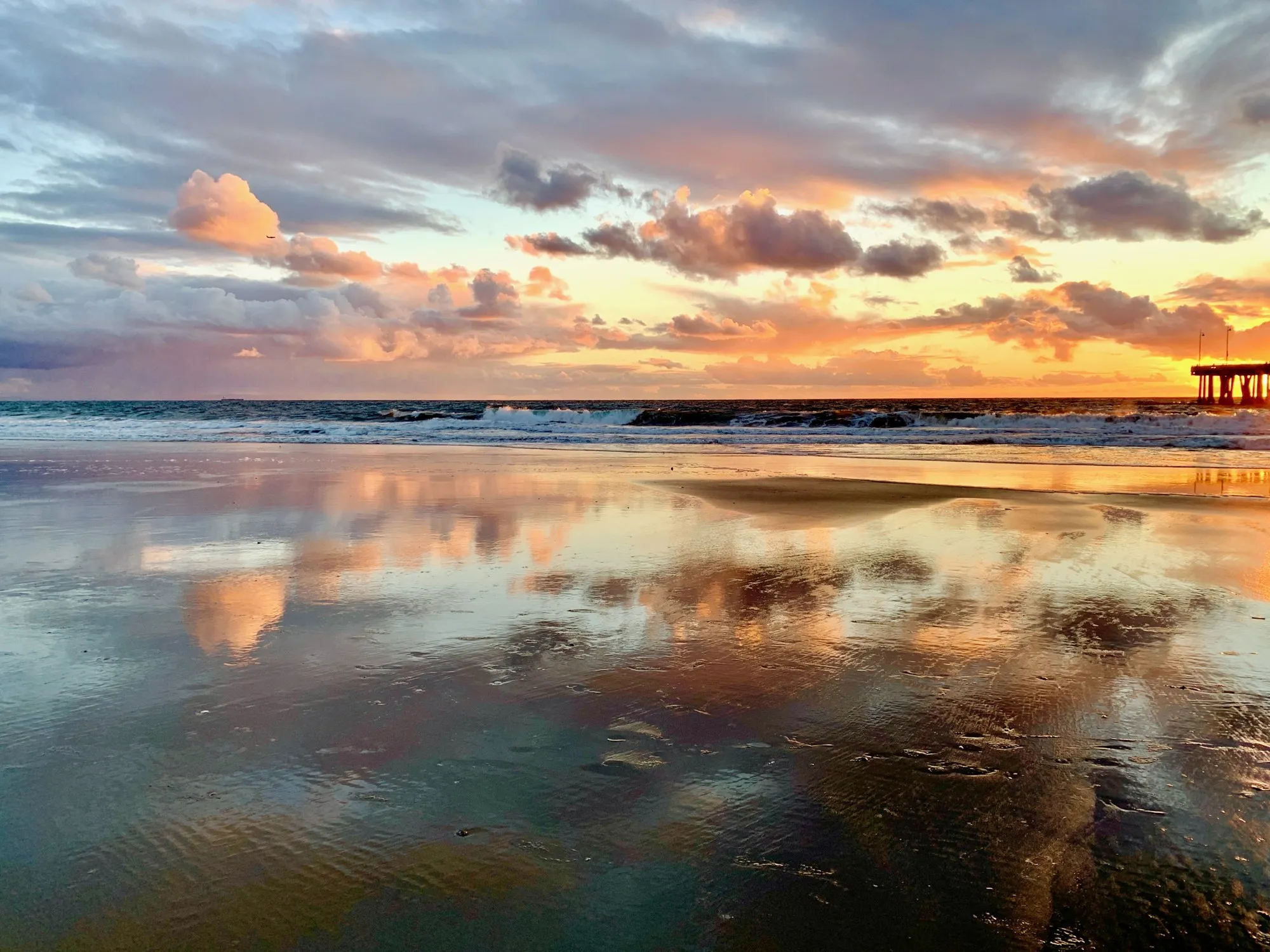 The ocean horizon and a pale sunset are mirrored across wet sand.