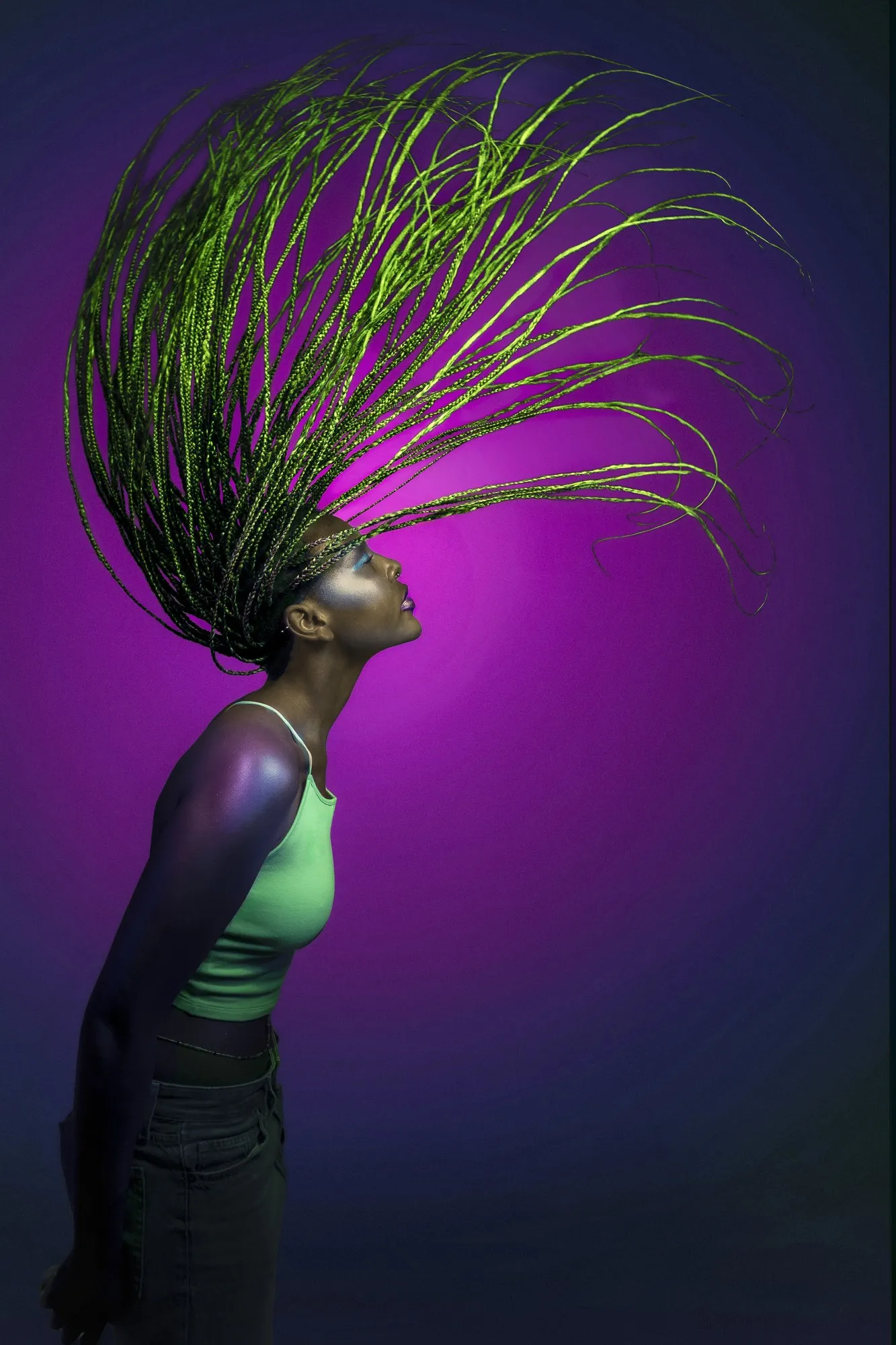 A dancer with an arcing headdress lit in purple and green against a dark background