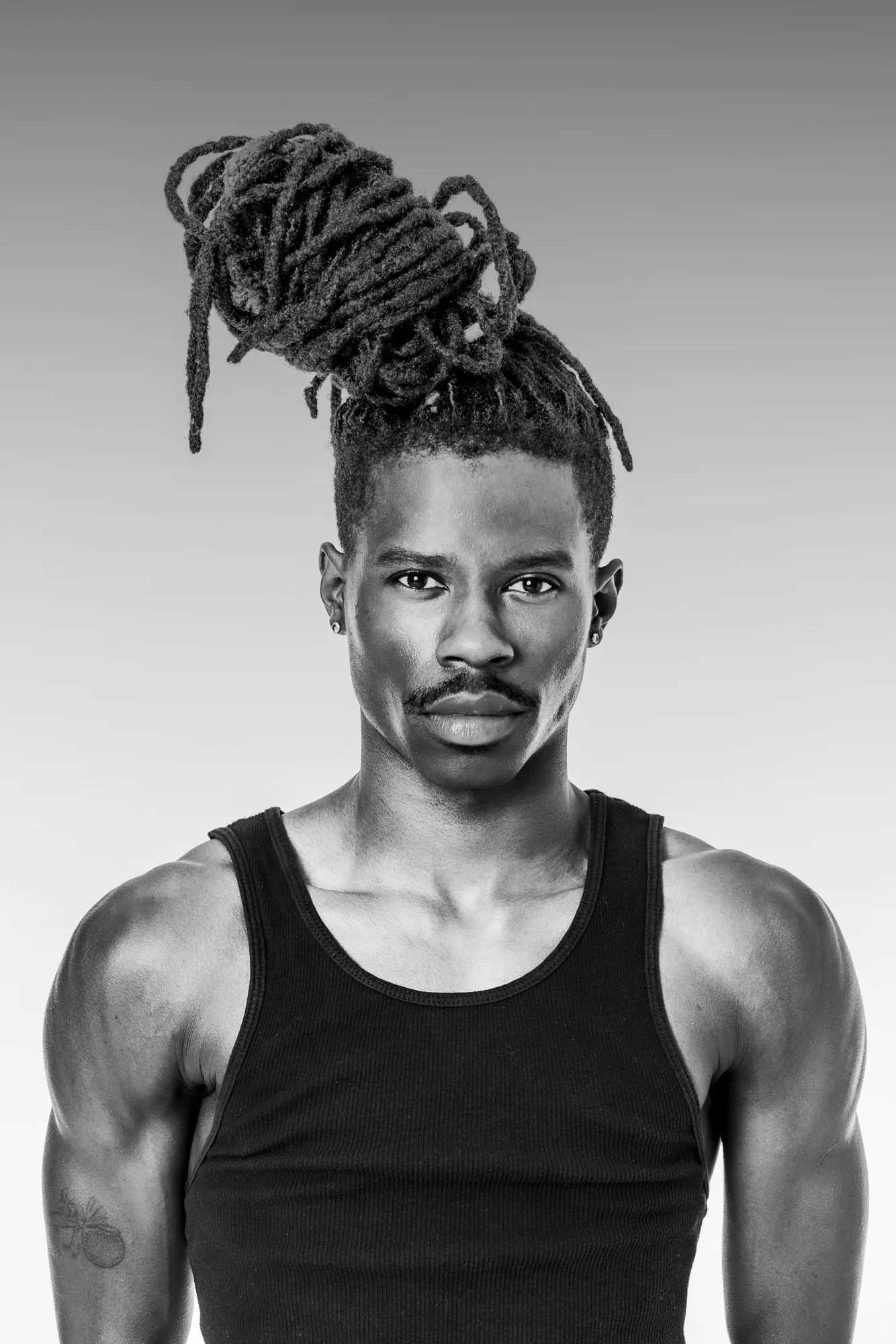 Black-and-white portrait of a man wearing his locs in a high knot