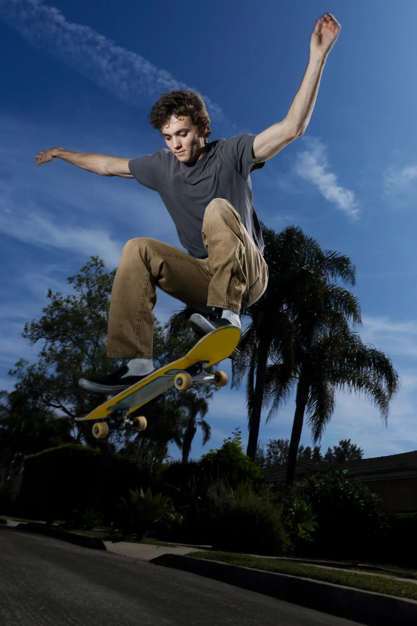 A skateboarder midair above a street lined with palm trees