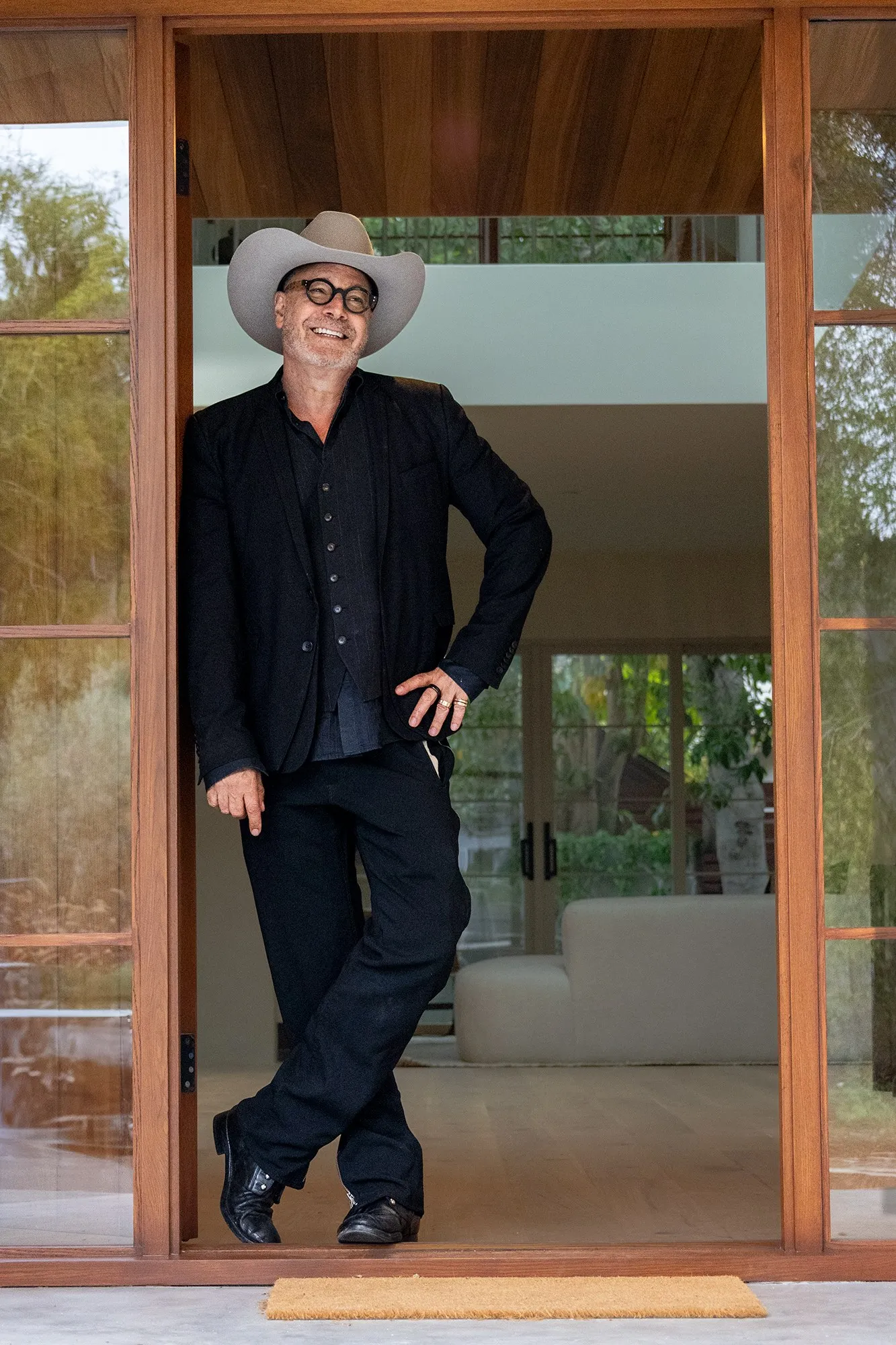 A man in a hat standing in a doorway with his ankles crossed
