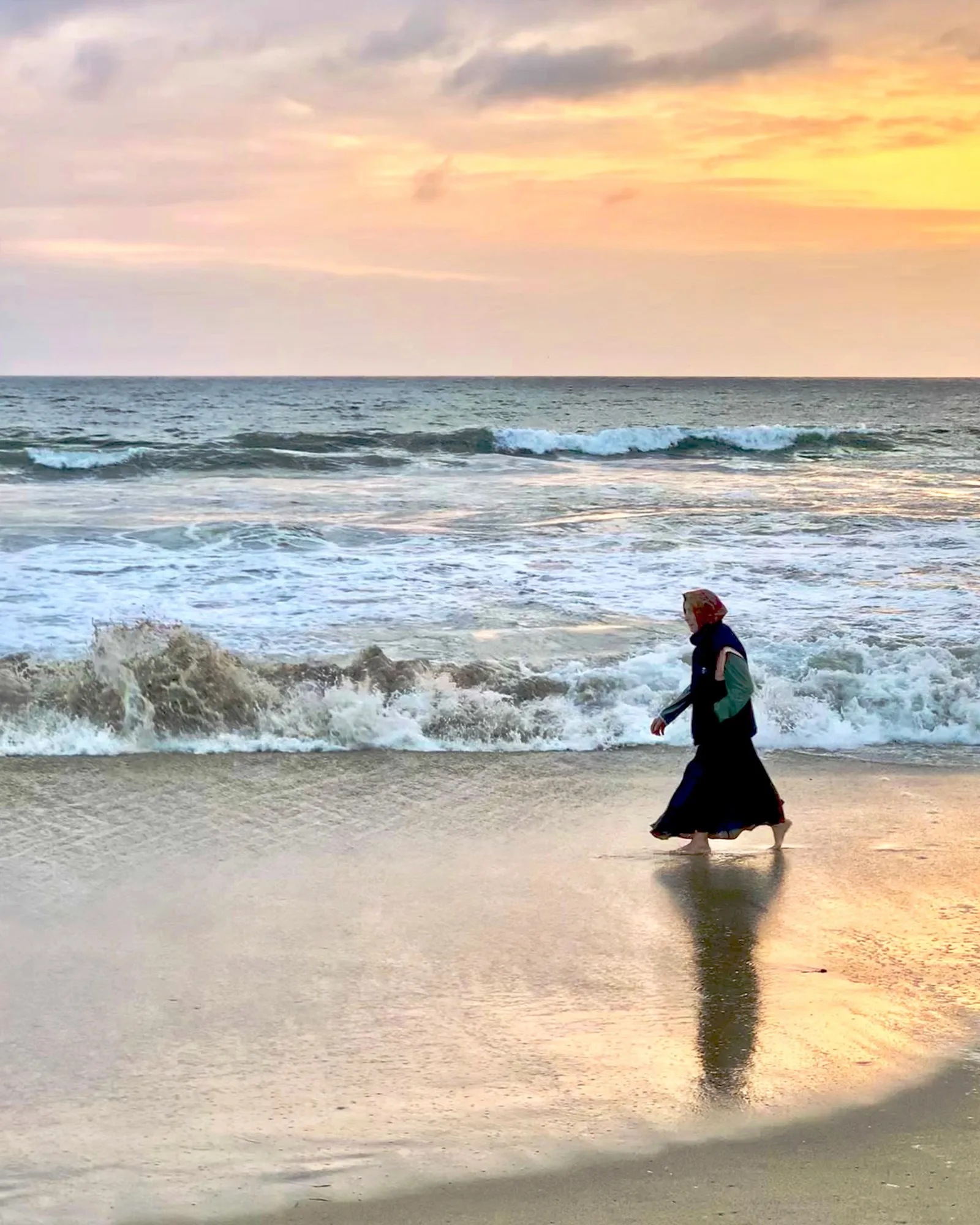 A person walks into the ocean as evening light glows on the water.