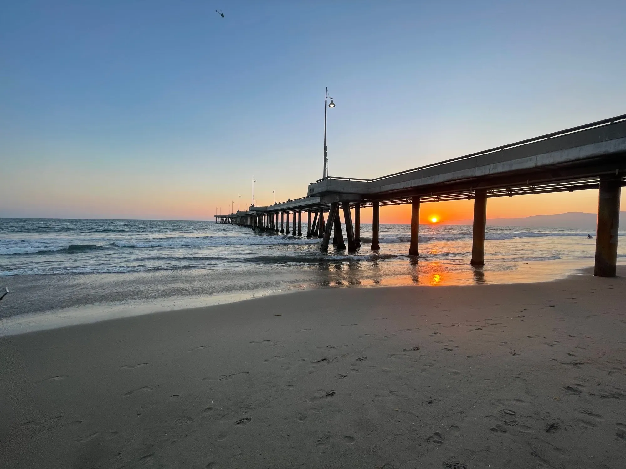 A pier crosses the beach as orange light falls between its supports.