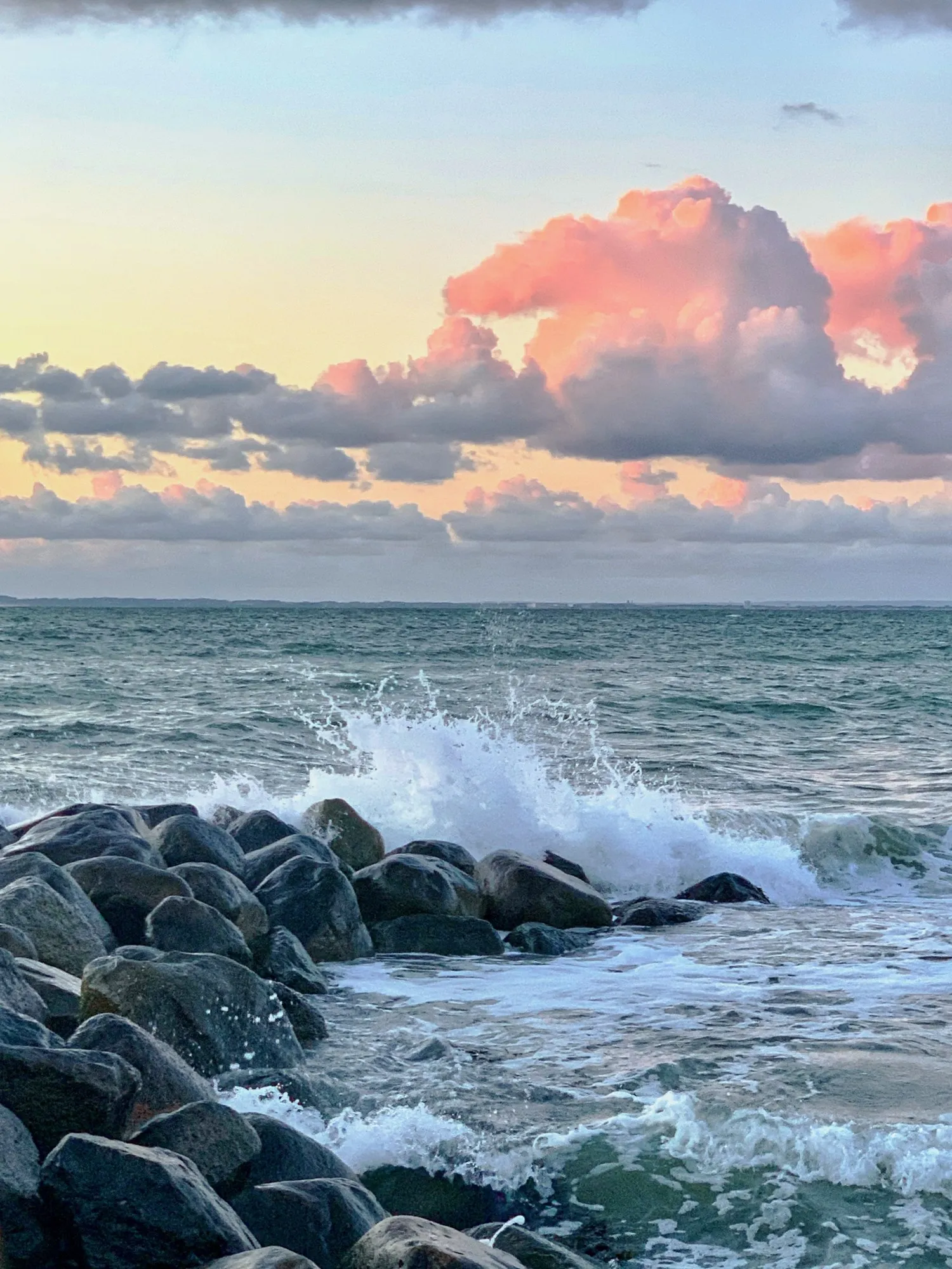 Pink clouds gather over a wide stretch of breaking waves.