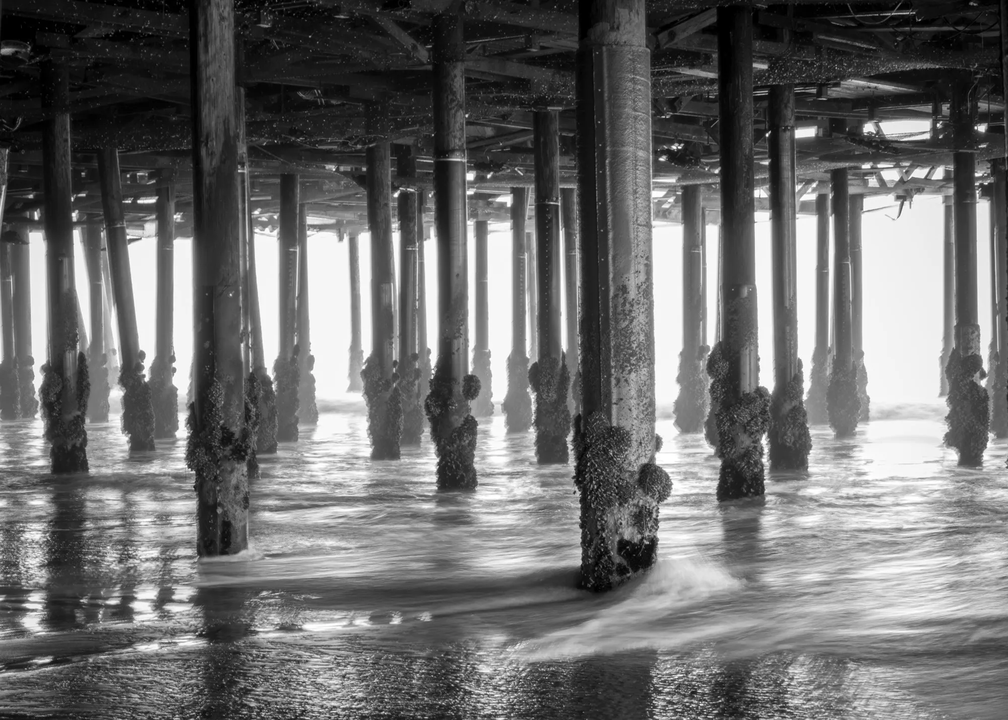 Black-and-white view through repeating pier columns above moving water