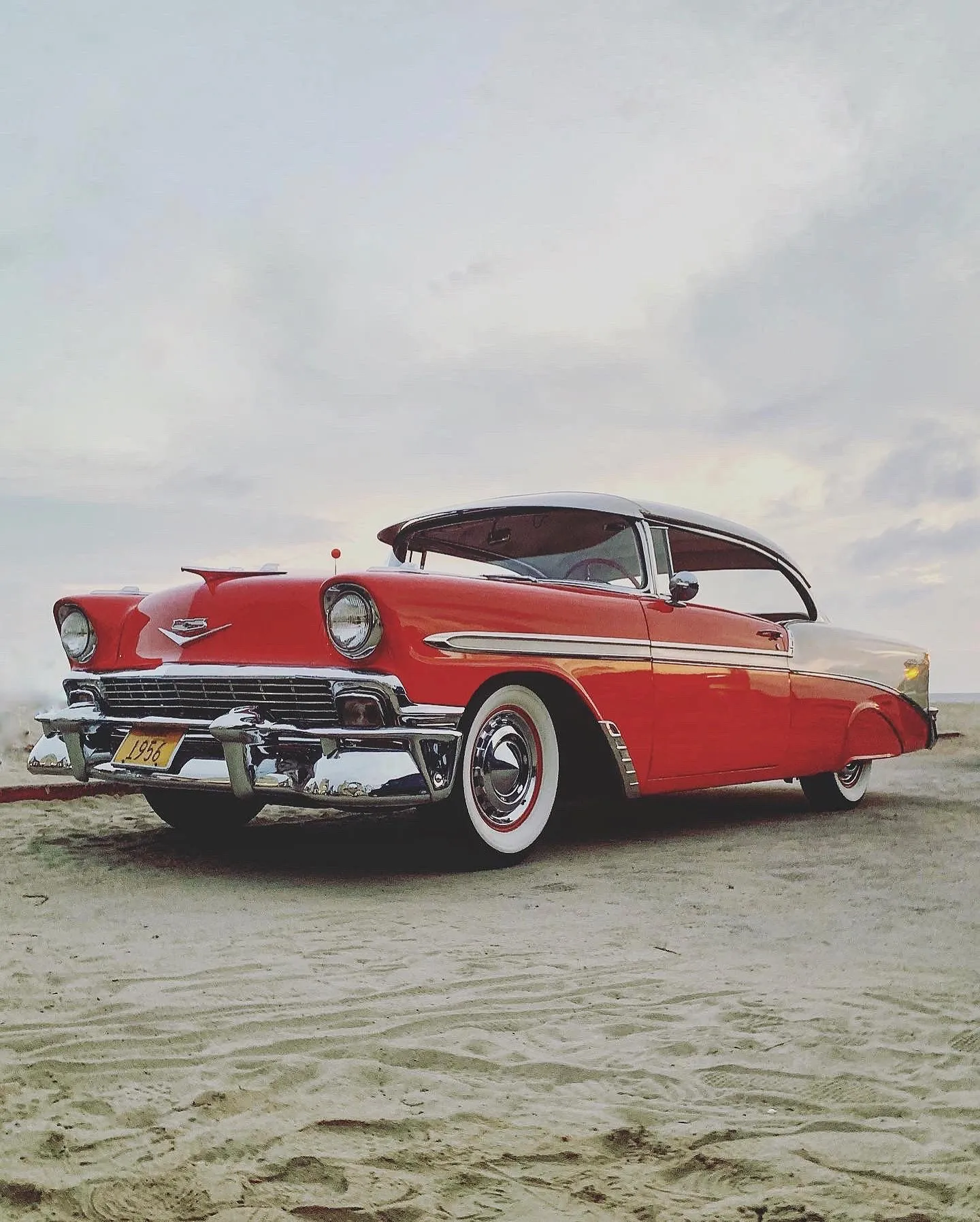 A red classic Chevrolet photographed low against a pale beach sky