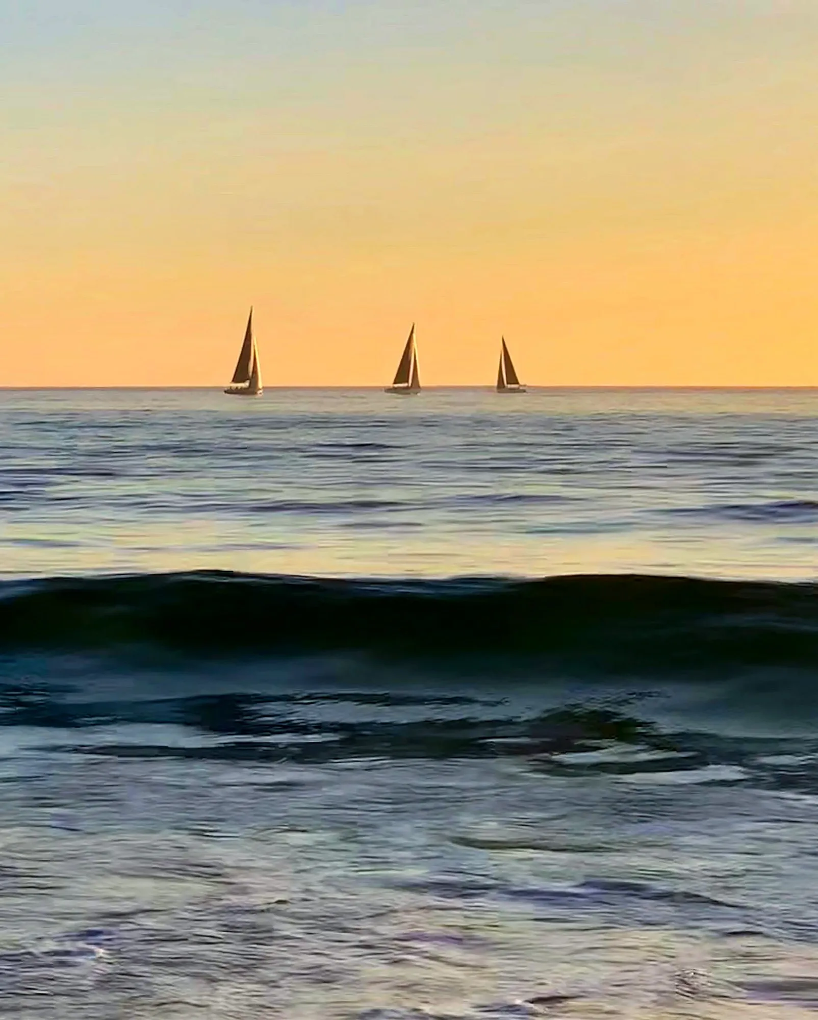 Small sailboats against a golden horizon above dark ocean waves