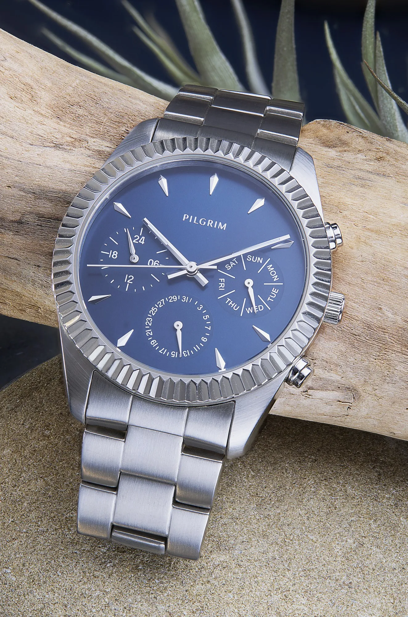 A silver Pilgrim watch with a blue face resting on driftwood