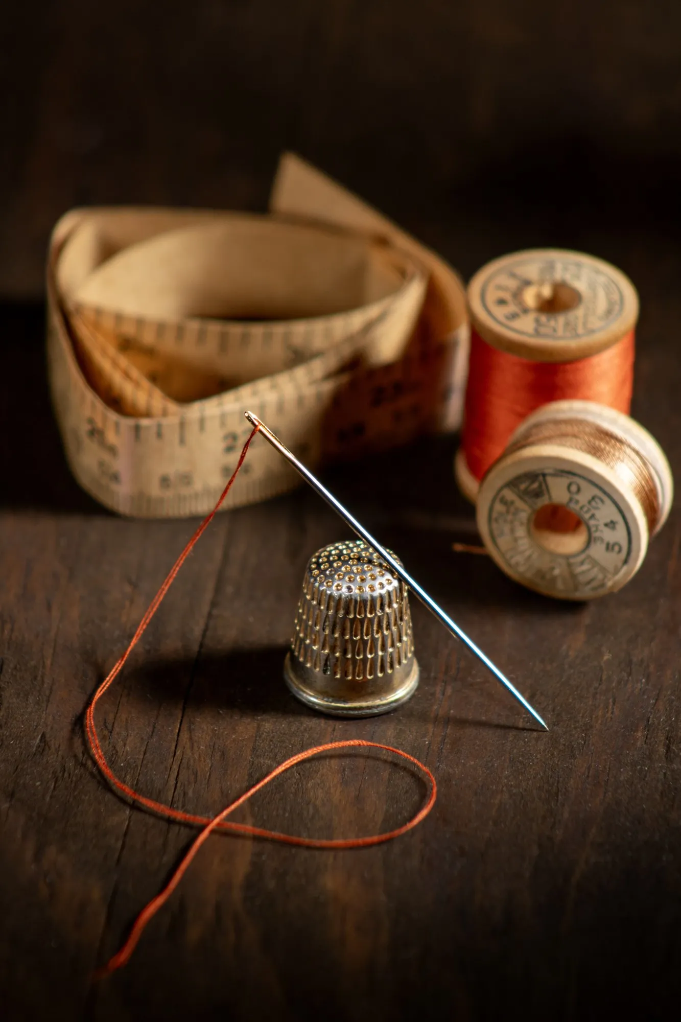 Thread spools, a thimble and a needle on a warmly lit sewing table