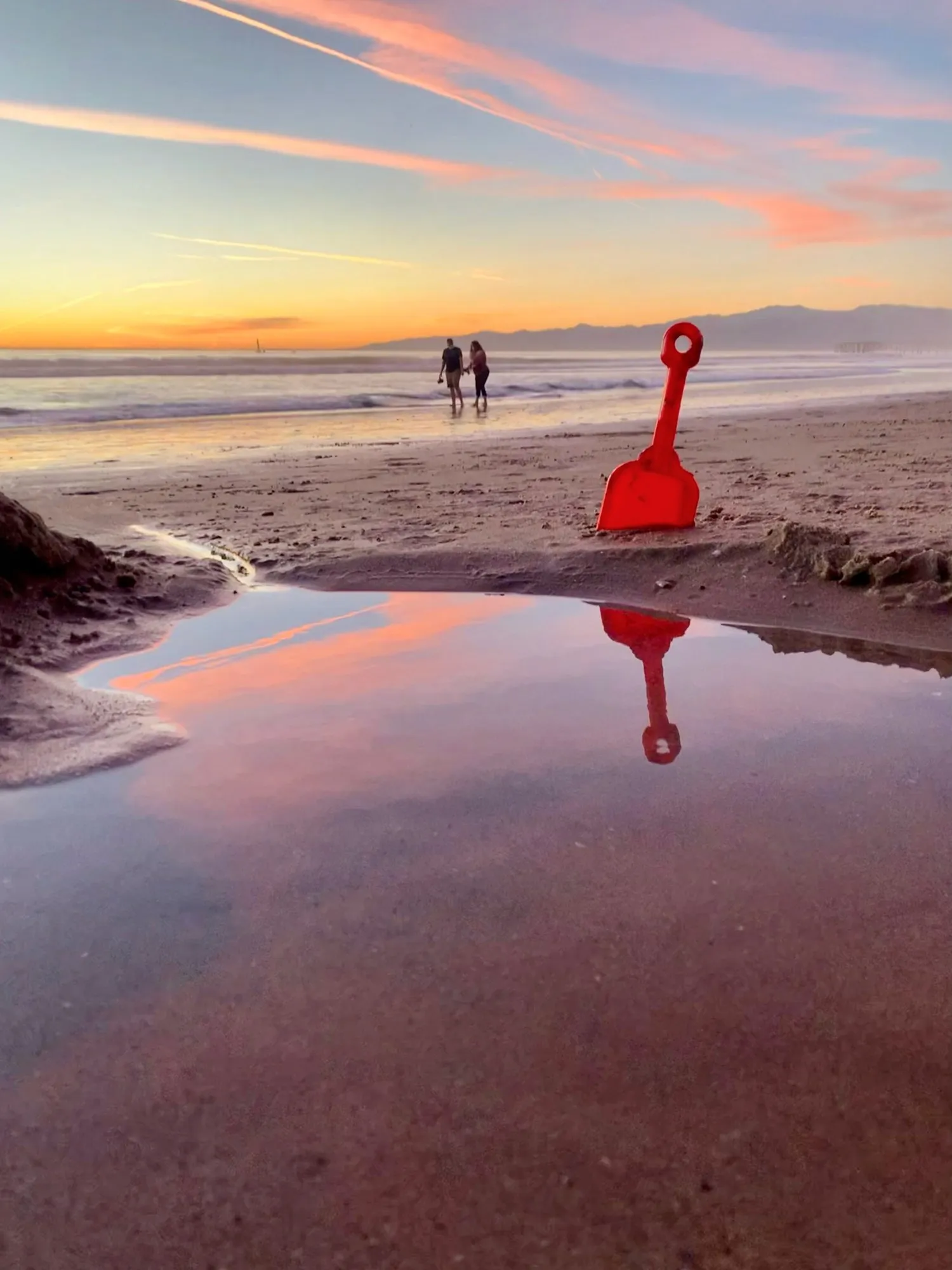 A red figure reflected at the shoreline. A beach observation made in the changing evening light.