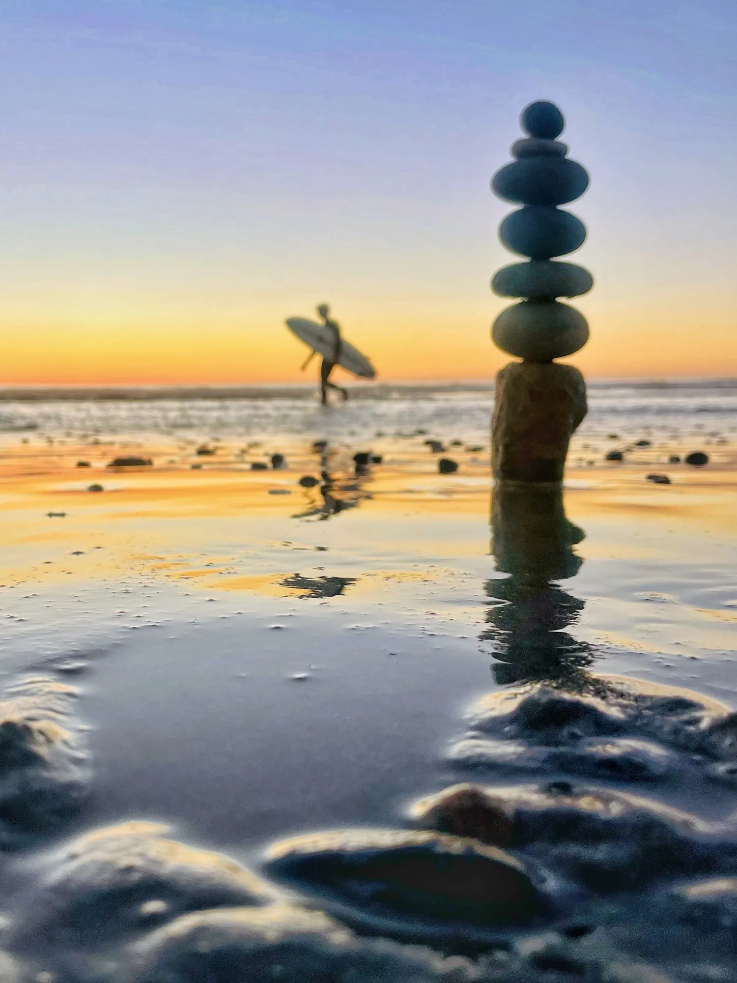 A stone tower reflected in wet sand with birds flying nearby