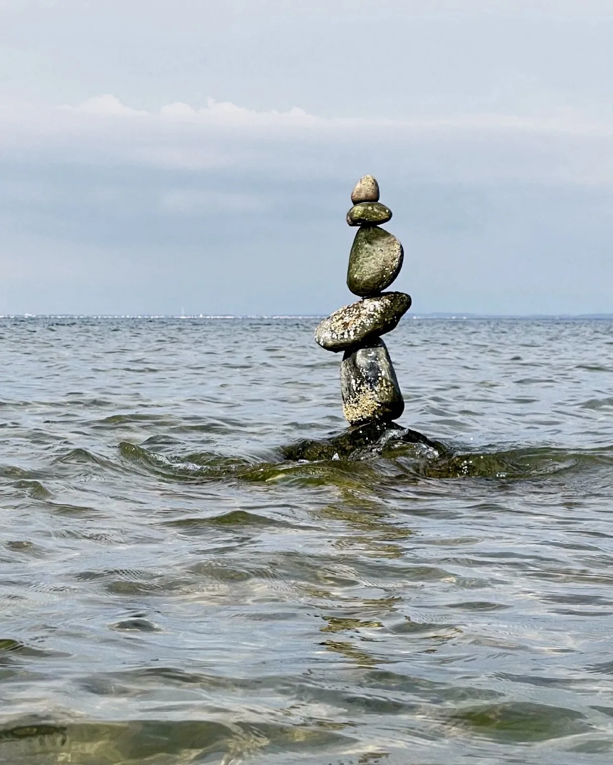 A slender stone stack rises from the water beside the open sea.