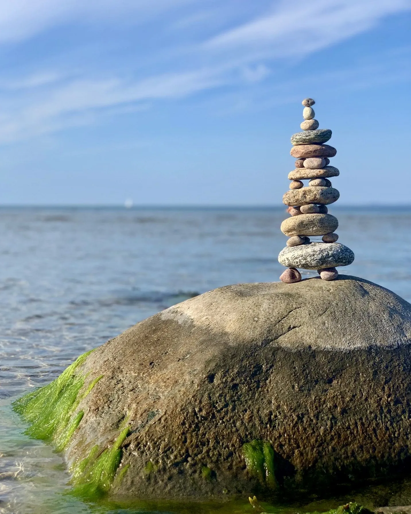A small balanced stone stack sits on a green shoreline boulder.
