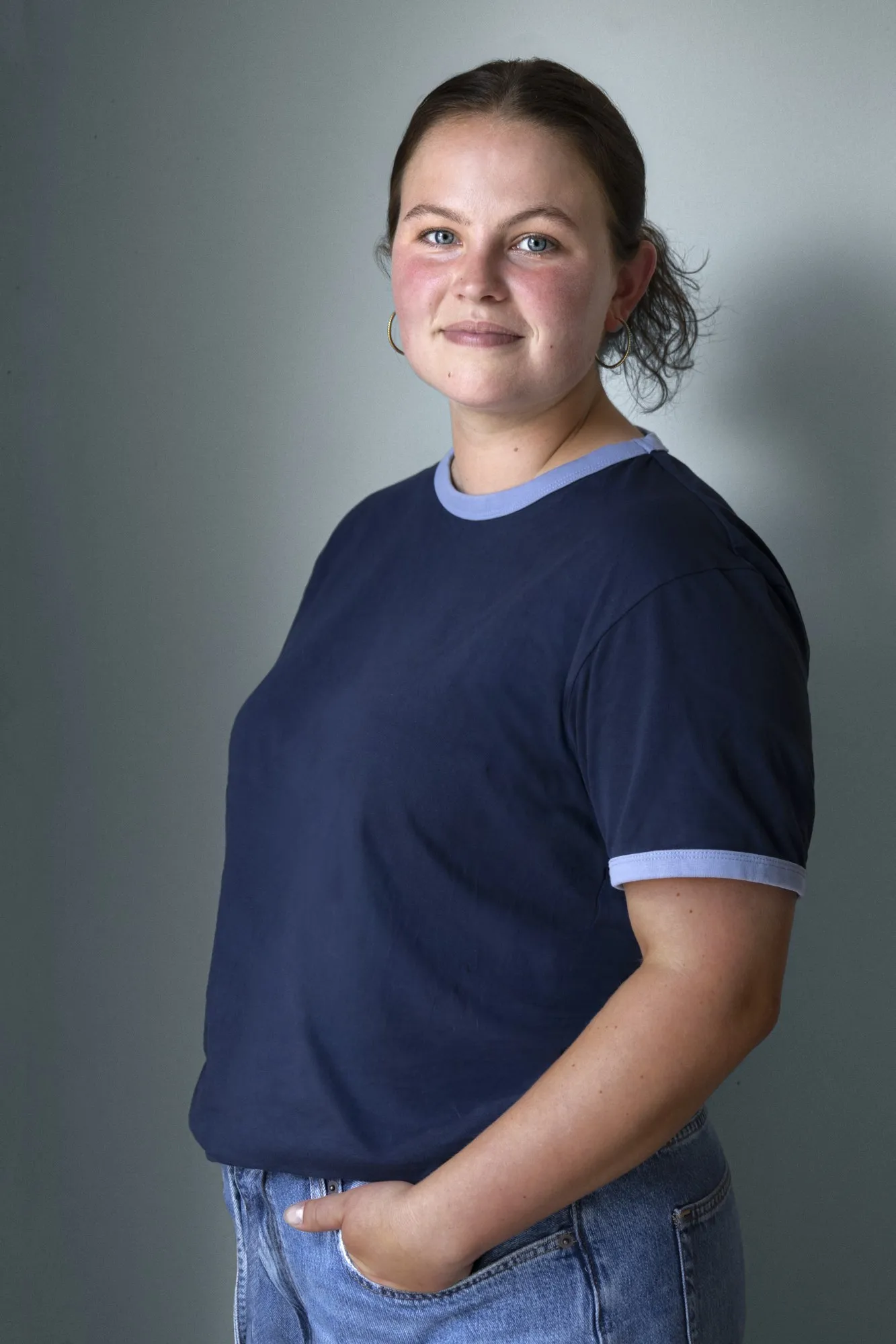 A smiling teenage girl in a navy polo poses against a soft gray studio background.