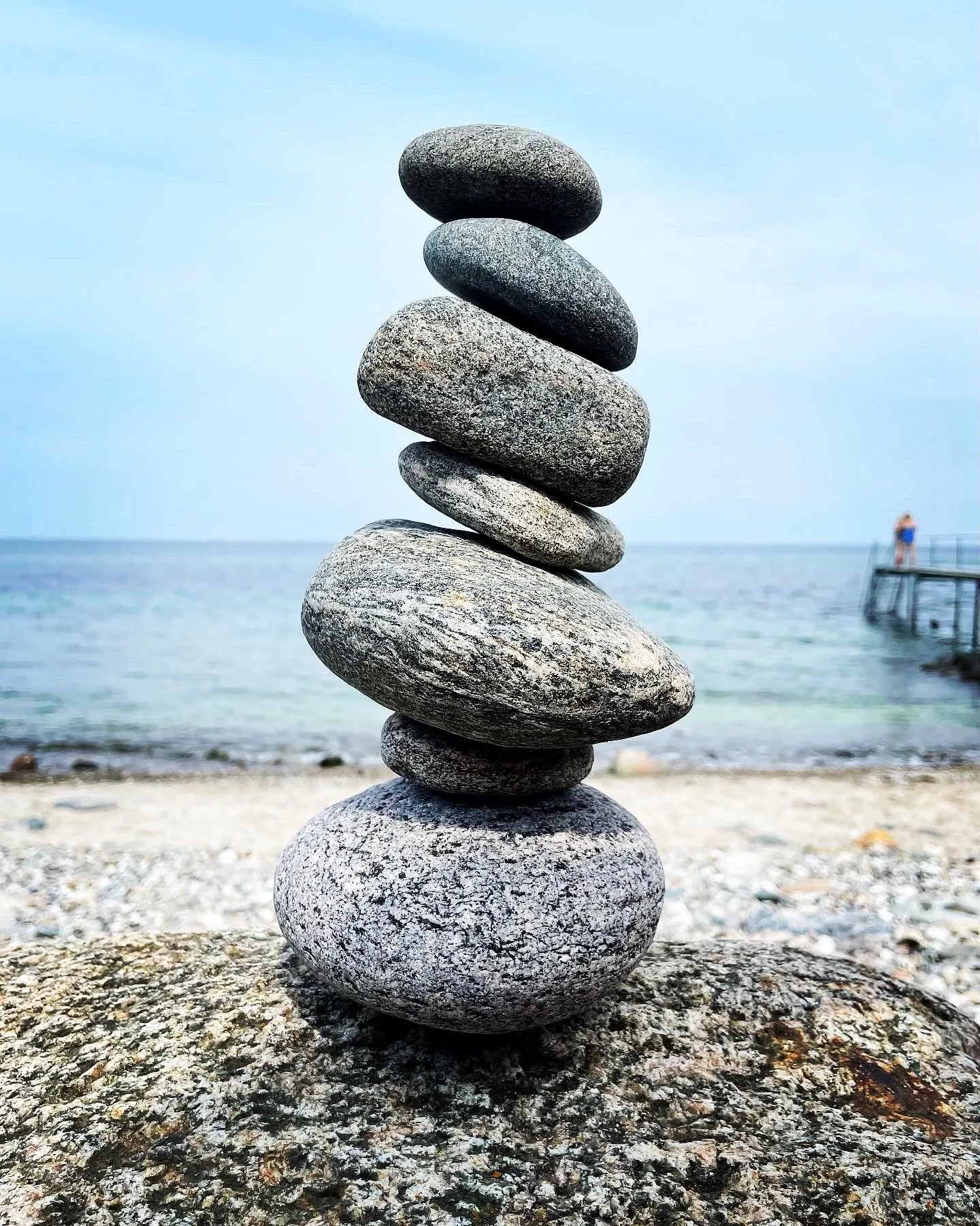 A smooth stone tower balances above the pebbled beach in soft daylight.