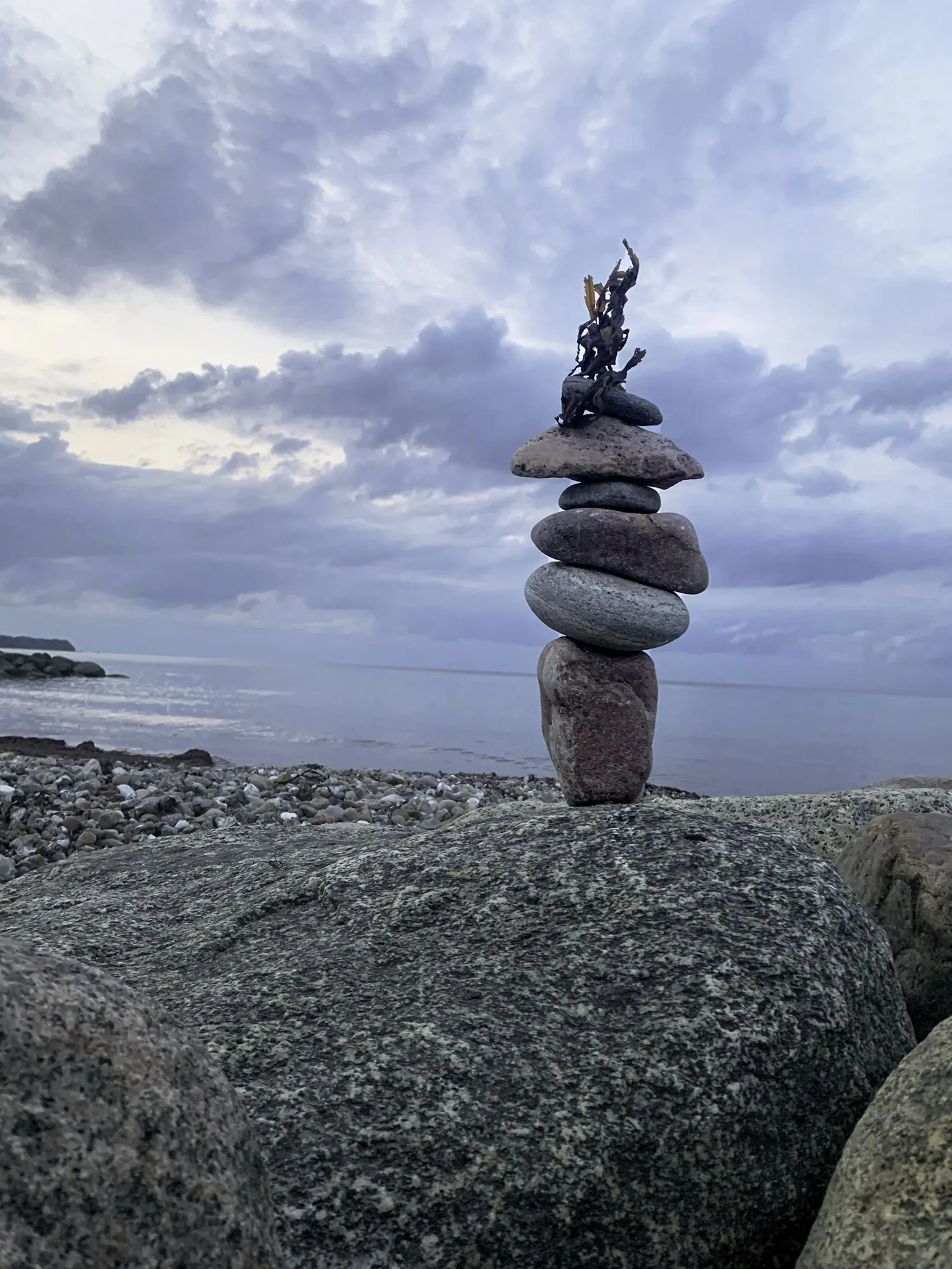 A stone cairn rises from dark shoreline rocks beneath a dramatic clouded sky.