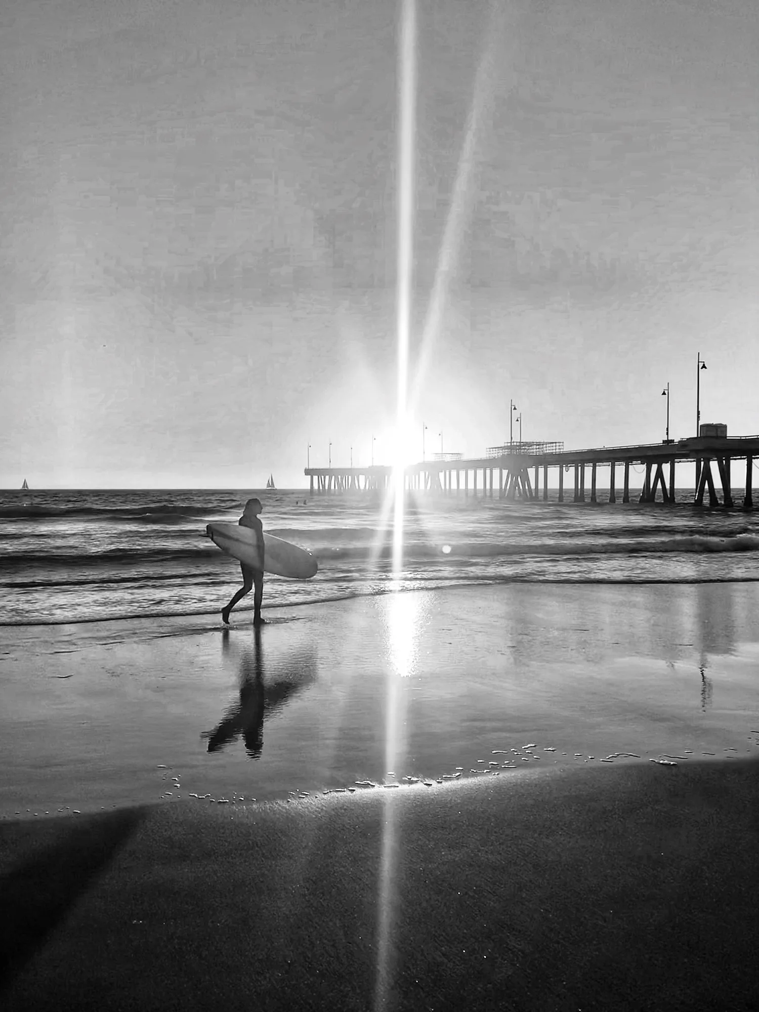 Black-and-white surfer and board beside a sunlit pier