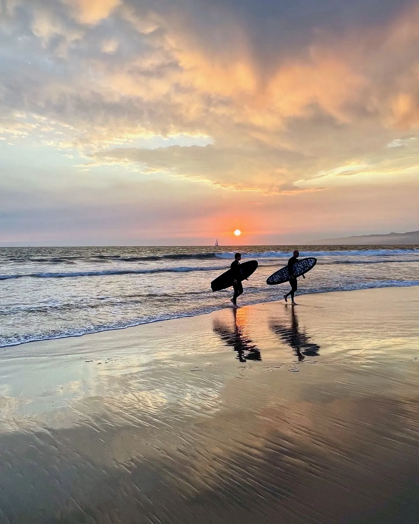 Two surfers reflected in the water beneath luminous evening clouds