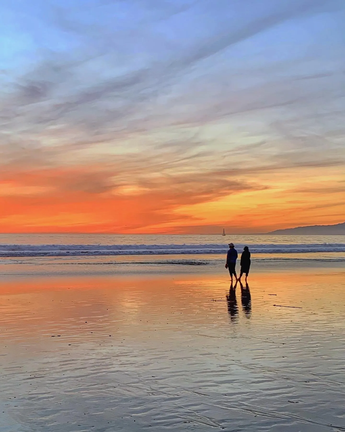 Two figures reflected in the water. A beach observation made in the changing evening light.