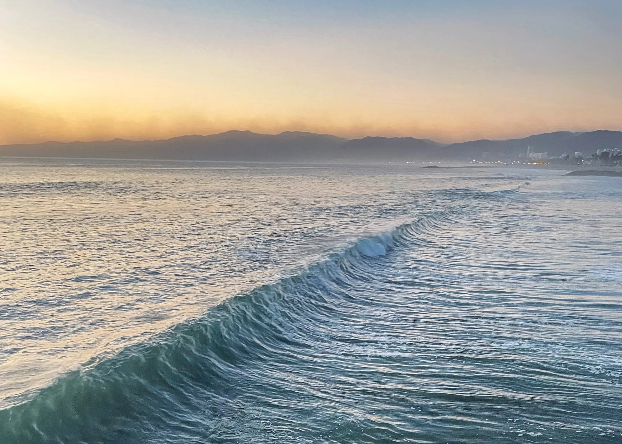 A wave curls toward the shore. A beach observation made in the changing evening light.