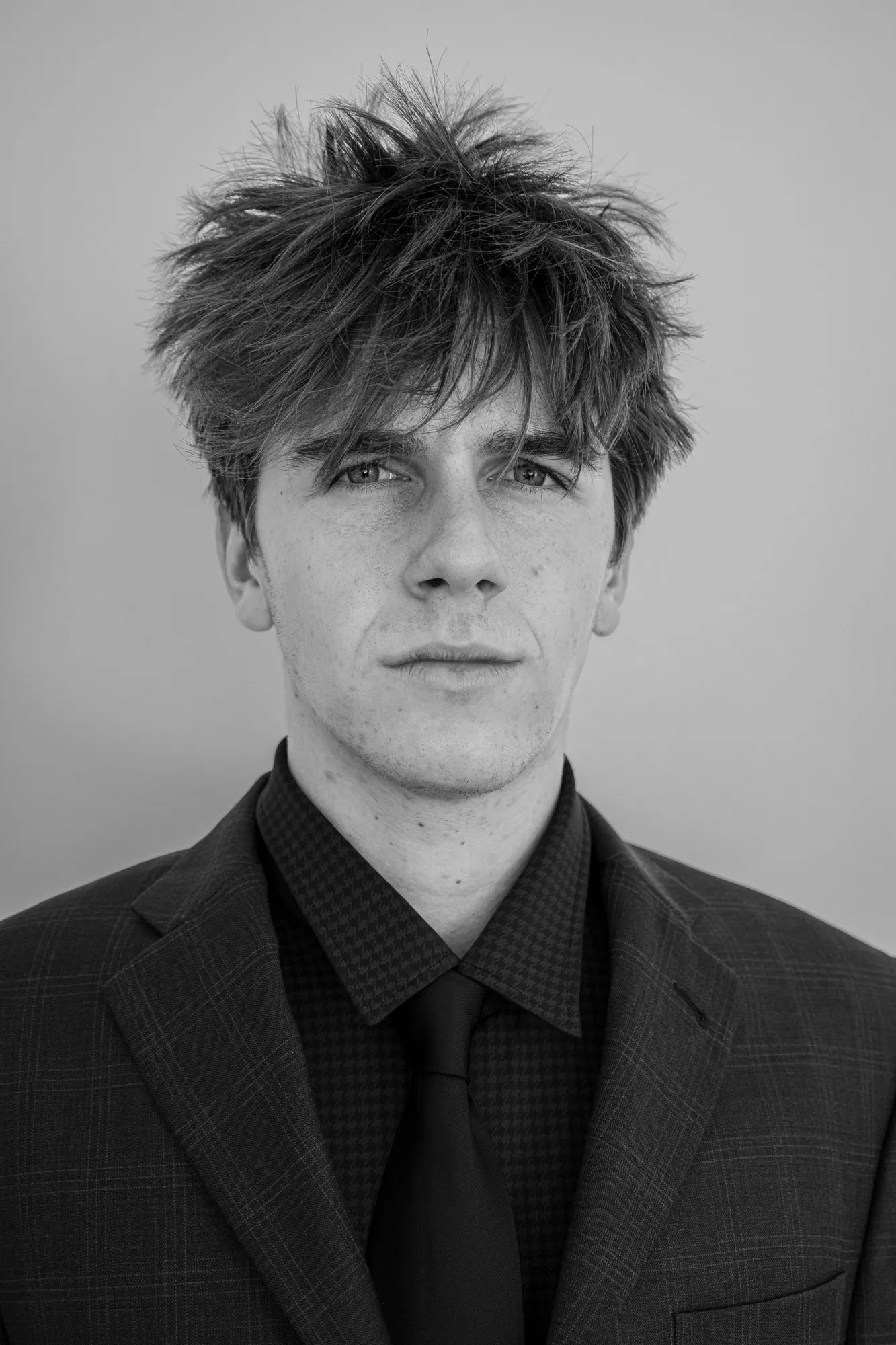 A young man in a dark jacket poses against a pale studio background.