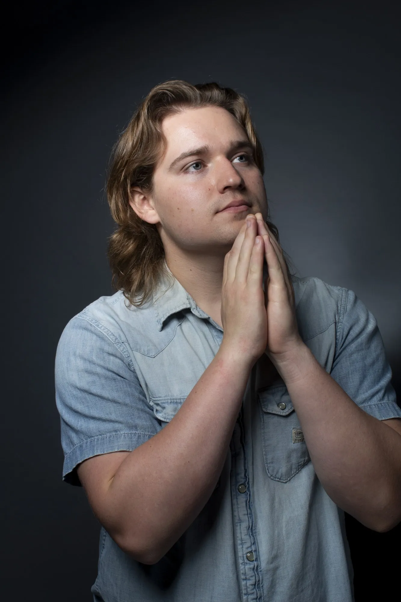 A young man in a pale shirt holds his hands together beneath a clear blue sky.